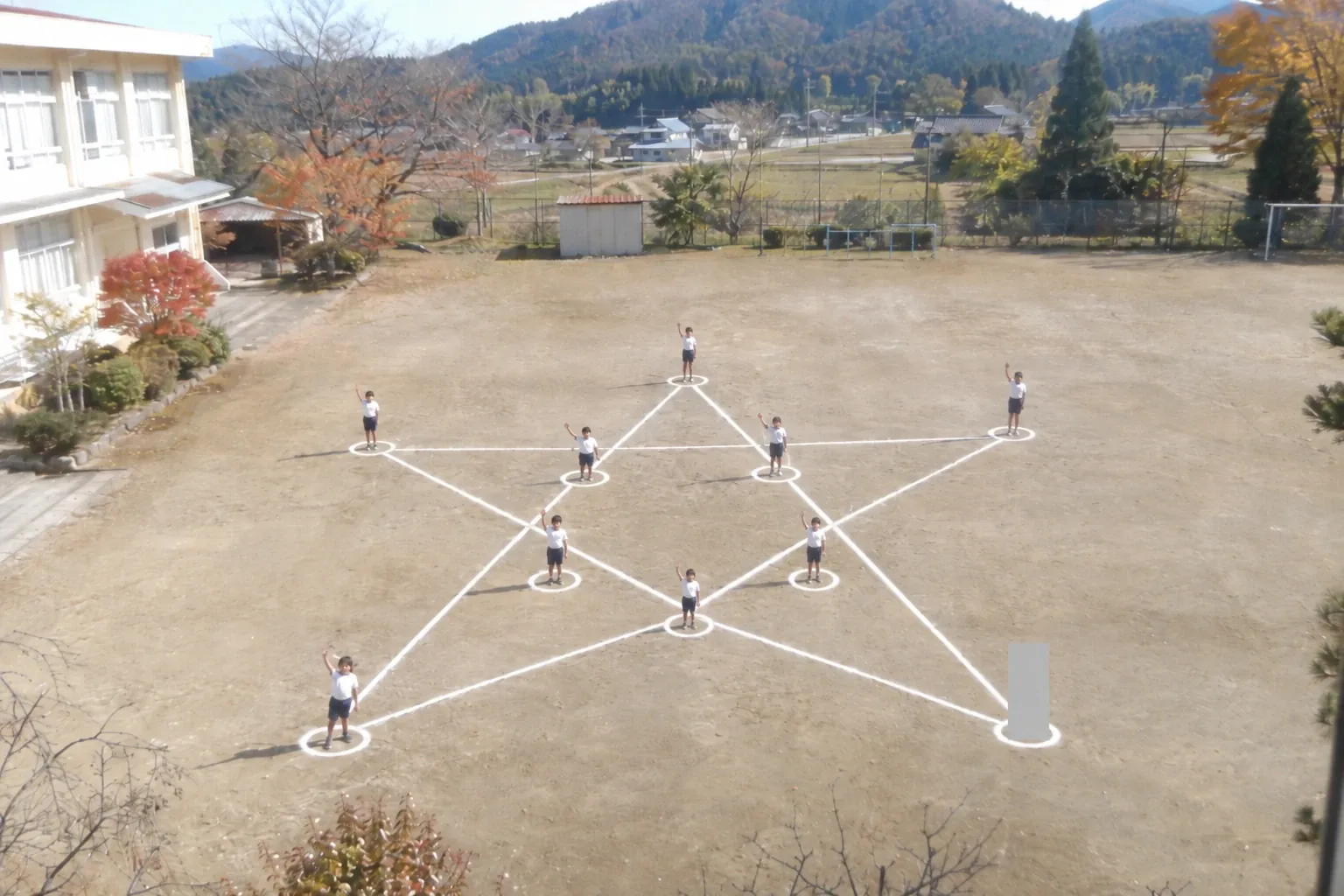 校舎の二階から見下ろした校庭。白線で描いた星の形の上に、児童が九人立って手を振っている。右下の一か所だけが、四角く灰色に塗りつぶされている。