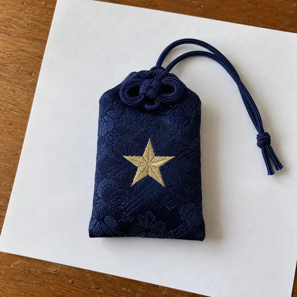 白い紙の上に置いた、星の刺繍の藍色のお守り